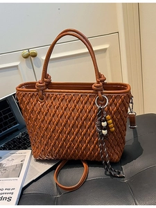 Brown woven bucket bag with double handles and tassel charm in a lifestyle setting