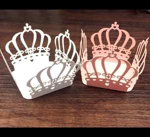 Laser-cut crown cupcake wrappers in white and pink on dark wood surface