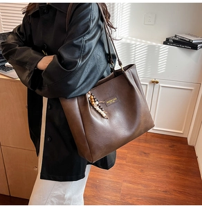 Détail du sac cabas en cuir marron foncé avec breloque perlée et étiquette de marque