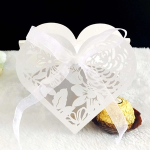 Detail showing white heart-shaped laser-cut wedding favor box with a white organza ribbon bow