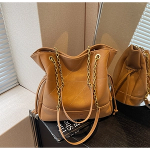 Detail of tan leather bucket bag featuring chain straps and quilted stitching design