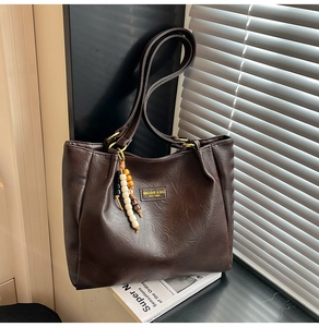 Détail du sac cabas vintage en cuir marron avec pompon décoratif et écusson de la marque