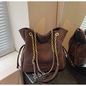 Detail of coffee brown suede bucket bag with gold chain strap and drawstring closure