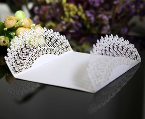 Detail view of laser-cut white wedding invitation envelope with intricate floral lace pattern