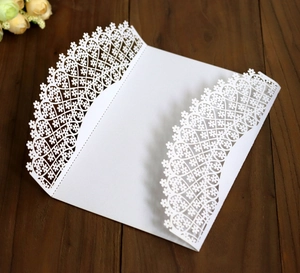 Intricate laser-cut white floral heart wedding invitation on dark wood surface