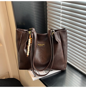 Détail du sac cabas marron foncé avec pendentif en perles et texture cuir vintage en lumière