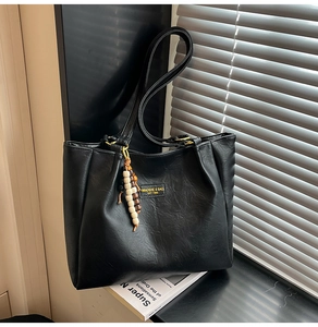 Détail du sac cabas en similicuir noir avec breloque en perles et logo embossé