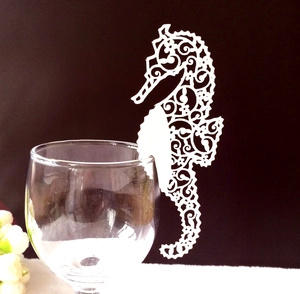 White laser-cut seahorse place cards for glass decoration on a dark background