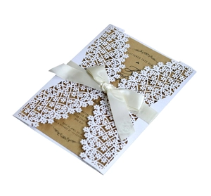 Detail of laser-cut floral lace wedding invitation with craft paper and cream ribbon