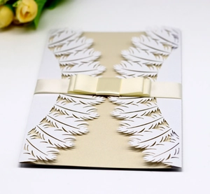 Detailed laser-cut white feather invitation card with elegant cream ribbon and gold lining