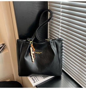 Détail d'un sac cabas noir en cuir avec pendentif en perles et écusson logo frontal