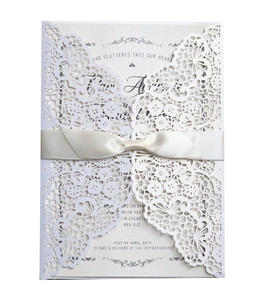 Elegant laser cut white lace wedding invitation with a cream silk ribbon bow and insert card
