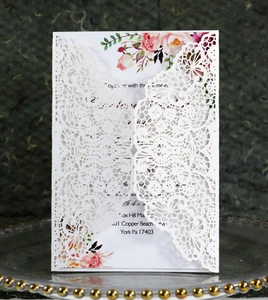 Detailed laser-cut lace pattern on white wedding invitation with floral insert