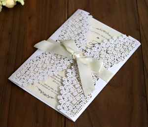 Macro detail of laser cut floral wedding invitation with beige ribbon bow on wood