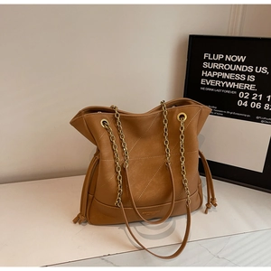 Detail of caramel quilted bucket bag with gold chain strap and brand logo lettering