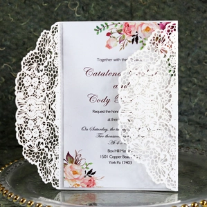 Close-up of laser-cut lace pattern and watercolor floral insert on white invitation