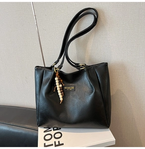 Détail du cabas en similicuir noir avec étiquette de marque et breloque décorative en perles