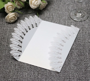 Close-up of white feather laser-cut wedding invitation card on textured gray fabric