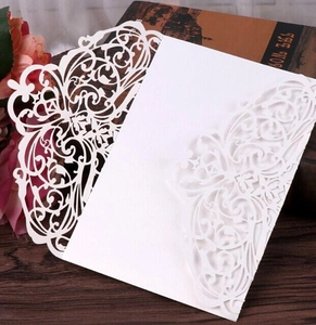 Intricate laser-cut floral pattern on white wedding invitation card on wood table