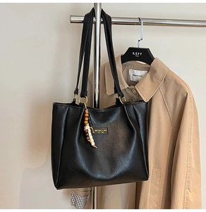 Gros plan sur un cabas en cuir noir avec logo métallique et pendentif en perles de bois