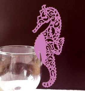 Pink seahorse laser-cut place card with hollow pattern clipped on a wine glass rim