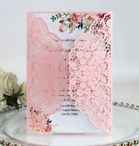 Detail of laser-cut lace wedding invitation with floral insert on elegant glass tray