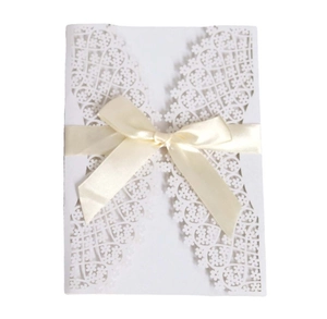 Detail of laser-cut floral hollow pattern on white wedding invitation with beige ribbon bow
