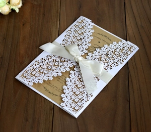 Detail of laser-cut lace wedding invitation with kraft paper insert and cream ribbon bow