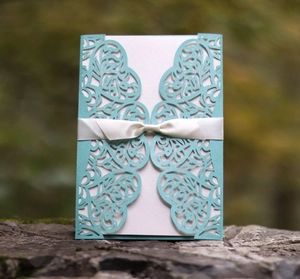 Detail of laser-cut filigree invitation card in light blue with white silk ribbon