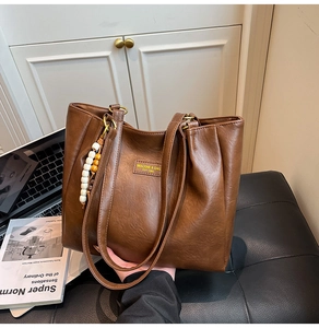 Gros plan sur un cabas en cuir marron foncé avec texture plissée et porte-clés perles