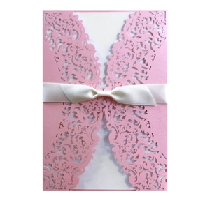 Detail of pink laser-cut lace wedding invitation with white silk ribbon and bow
