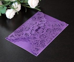 Detail showing the intricate laser-cut floral pattern on a dark purple invitation cover