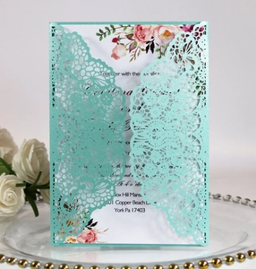 Close-up of laser-cut mint green wedding invitation with floral insert on glass tray