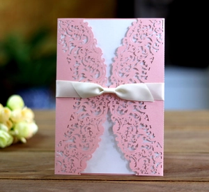 Detail of pink laser-cut wedding invitation with elegant white ribbon and lace floral design