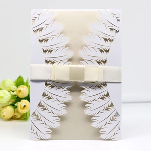 Laser-cut wedding invitation featuring white feather patterns and a champagne ribbon bow