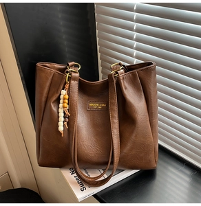 Détail du cabas vintage en cuir marron avec côtés plissés et perles en bois décoratives