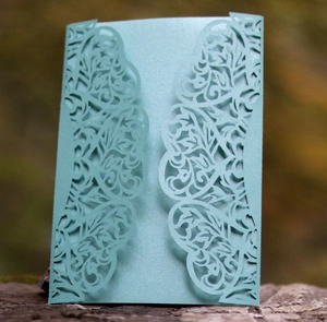 Macro view of laser-cut floral pattern on light blue pearlescent paper wedding card