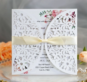 Detail of laser-cut lace wedding invitation with pink rose card and cream ribbon bow