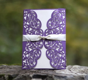 Detail of purple laser-cut wedding invitation with white ribbon on a natural stone base