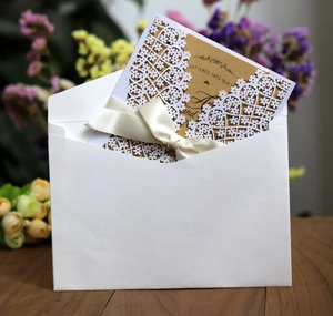Detail of laser-cut white floral wedding invitation with silk bow on wood background
