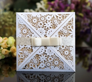 Macro detail of laser-cut floral wedding invitation with white paper and champagne ribbon