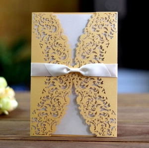 Close-up of golden laser-cut hollow lace wedding invitation with white silk ribbon bow