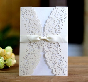 Detail of laser-cut ivory lace wedding invitation with an elegant satin ribbon bow