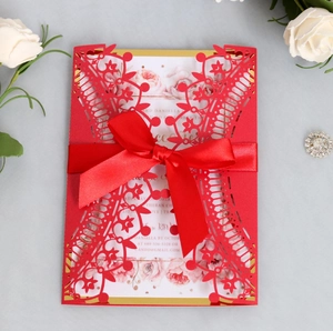 Detail of red laser-cut wedding invitation with satin bow and floral inner card