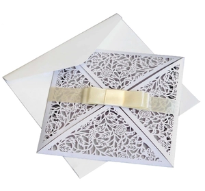Elegant white laser cut lace wedding invitation with a cream ribbon bow and envelope