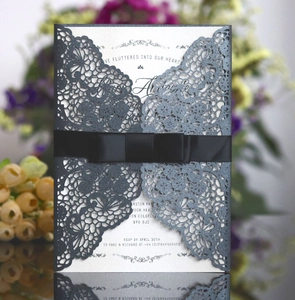 Macro shot of laser-cut lace wedding invitation with dark grey glitter and ribbon