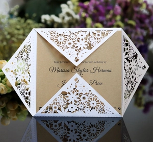 Laser-cut white floral wedding invitation with kraft paper insert on dark reflective surface