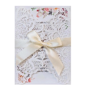 Elegant white laser-cut floral wedding invitation with cream satin bow and printed card
