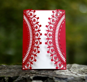 Intricate laser-cut floral patterns on a red wedding invitation card with forest background