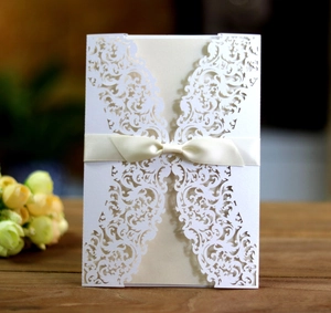 Detail of laser-cut white lace wedding invitation with a satin bow on wood surface